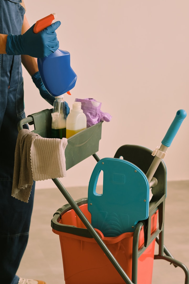 Main d’un(e) utilisateur(trice) tenant un flacon de produit de nettoyage près d'un chariot de ménage.